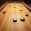 Top-down view of a digital table shuffleboard game with metal pucks sliding toward scoring zones
